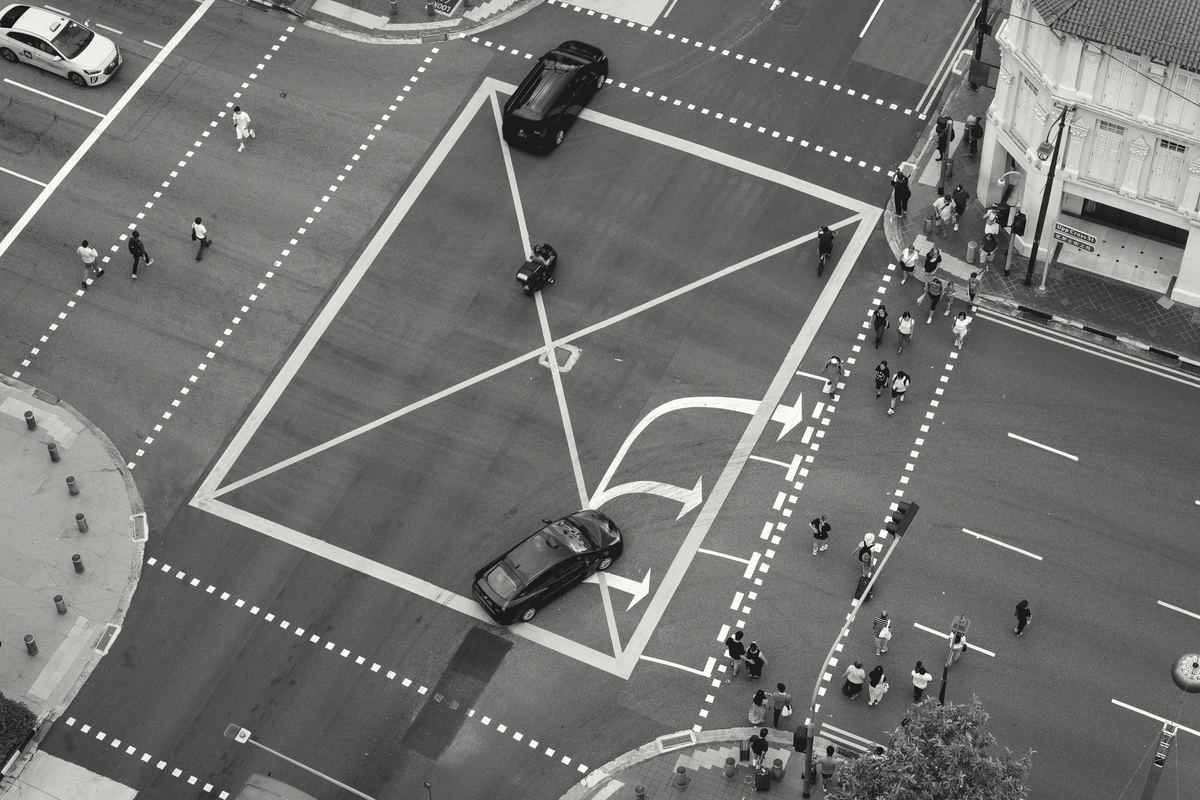 A junction in Singapore seen from above. Cars, a delivery rider and pedestrians move around a box marked on the road.